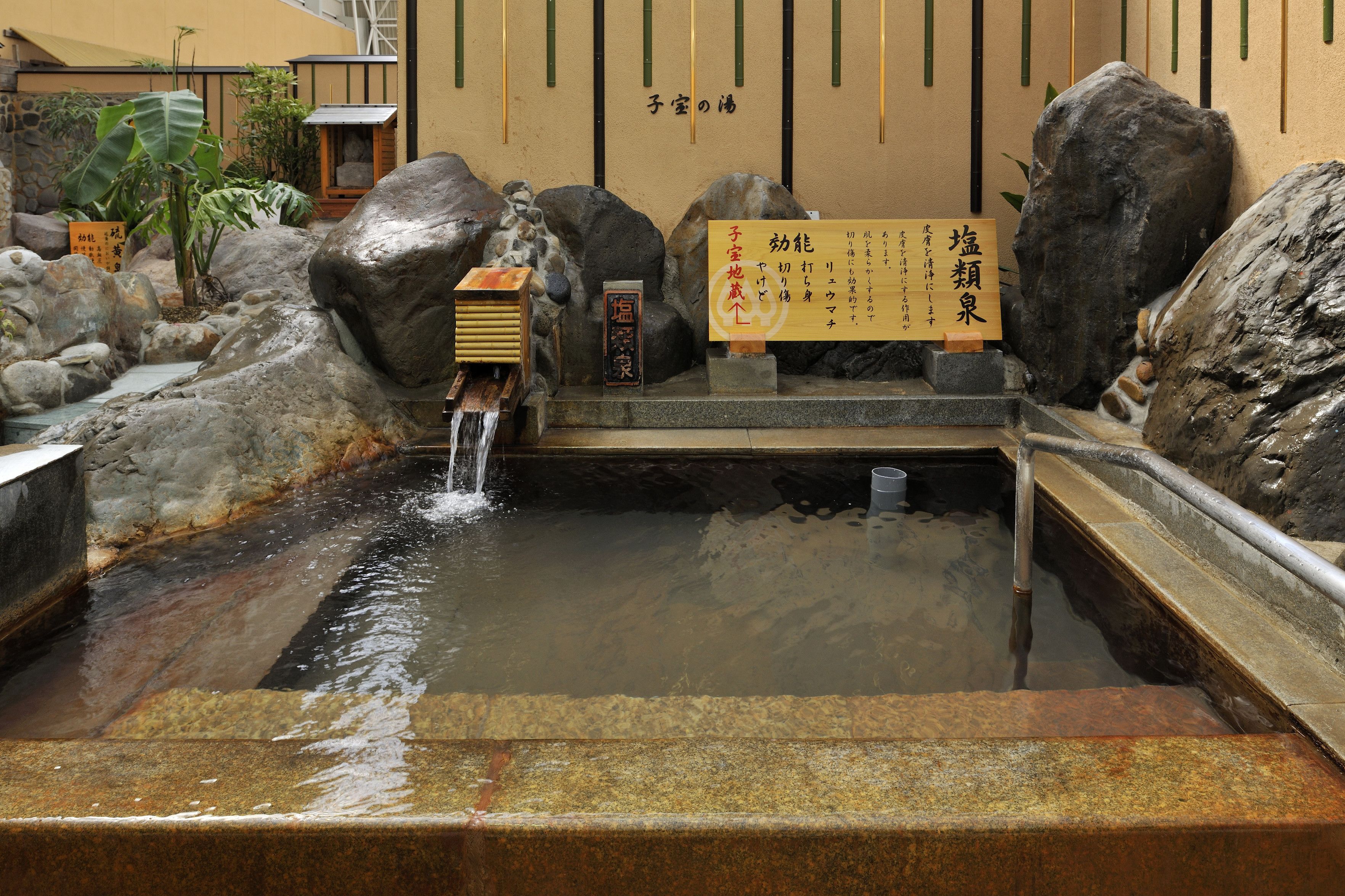 Un jardín japonés tradicional con un pequeño estanque, rocas y un letrero de madera con caracteres japoneses.