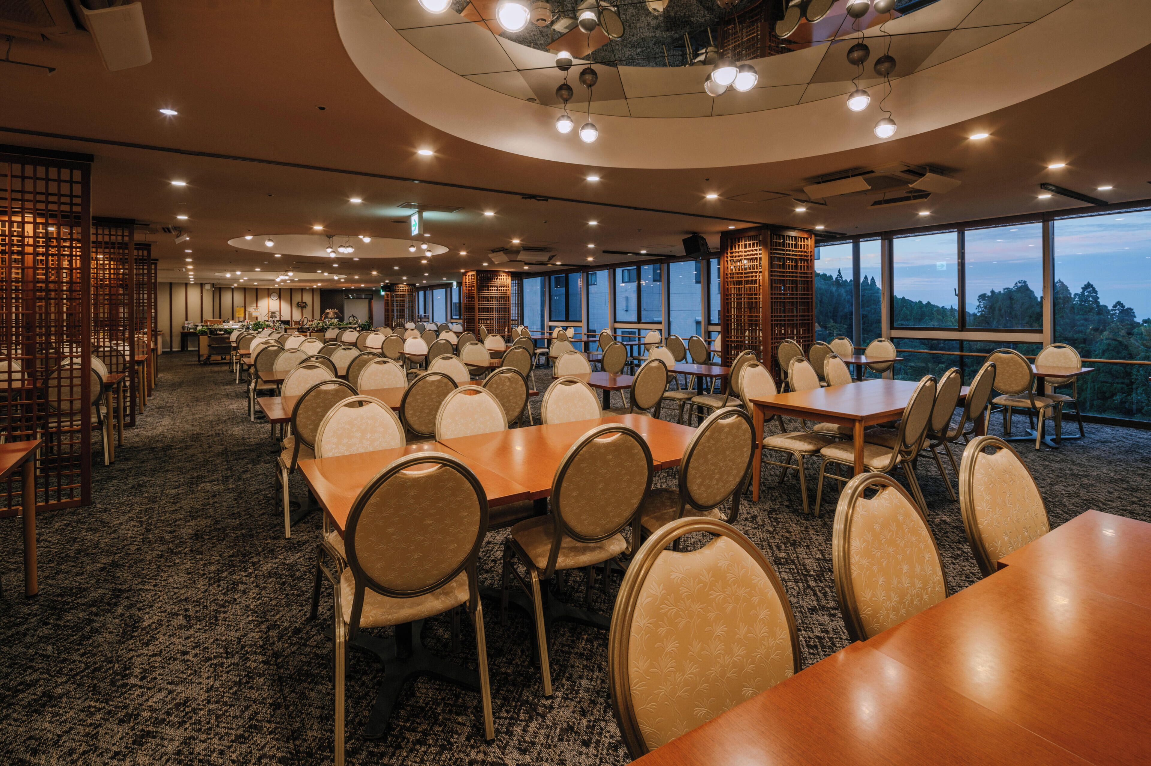 A conference room with multiple tables and chairs, large windows, and a high ceiling with recessed lighting.