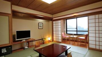 A traditional Japanese room with tatami flooring, a television, a table, and sliding doors.