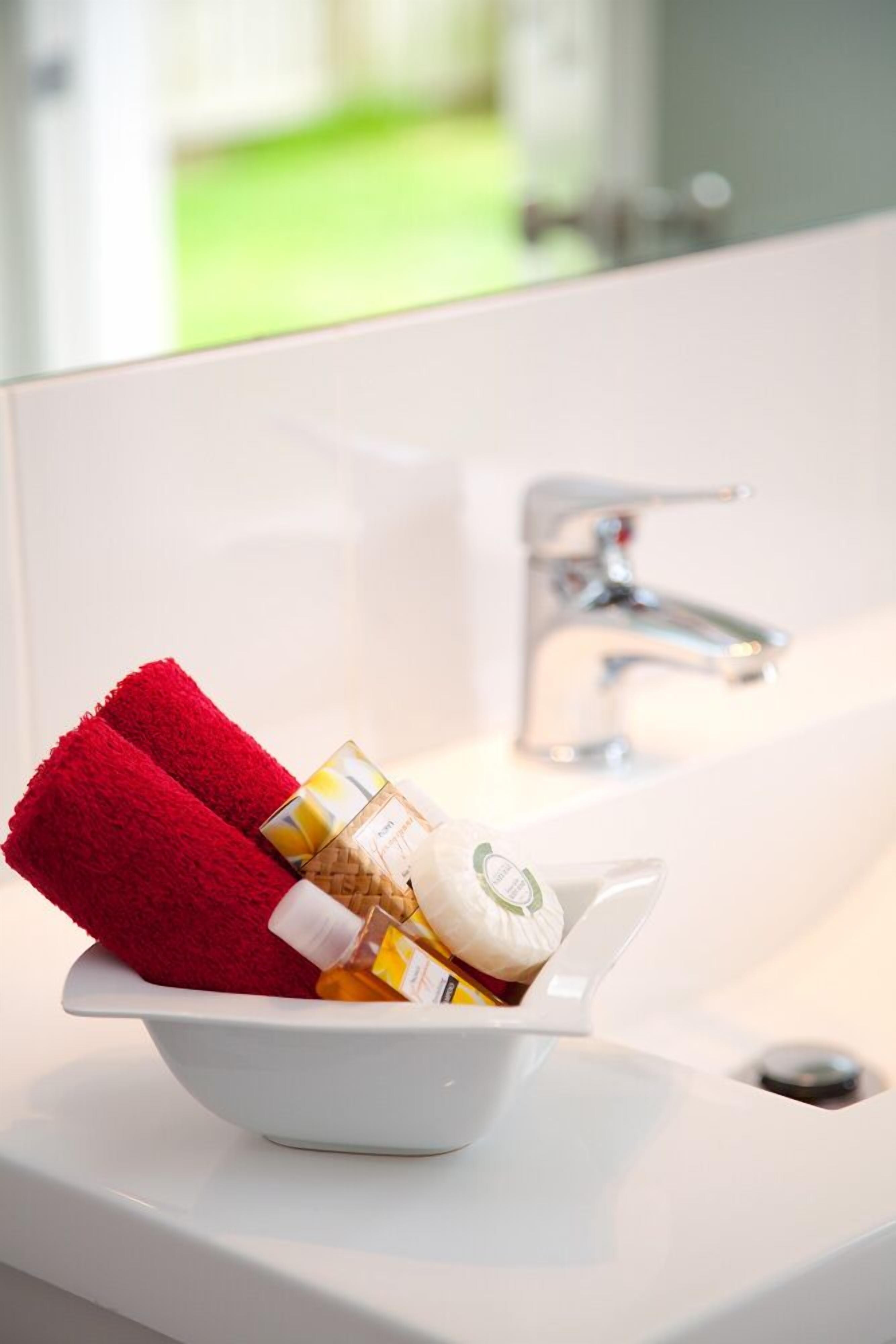 A white sink with a red towel and toiletries in a white bowl.