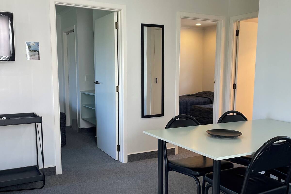 A hotel room with a dining table, chairs, a mirror, and a bed.