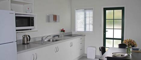 Uma cozinha moderna com armários brancos, uma pia de aço inoxidável, micro-ondas e uma área de jantar com mesa e cadeiras.