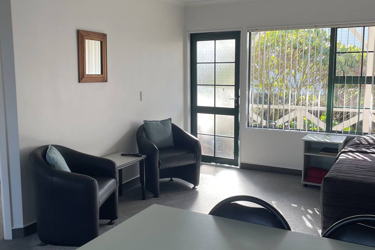 A modern room with a white table, two black armchairs, a small side table, a door with a view, and a window with blinds.