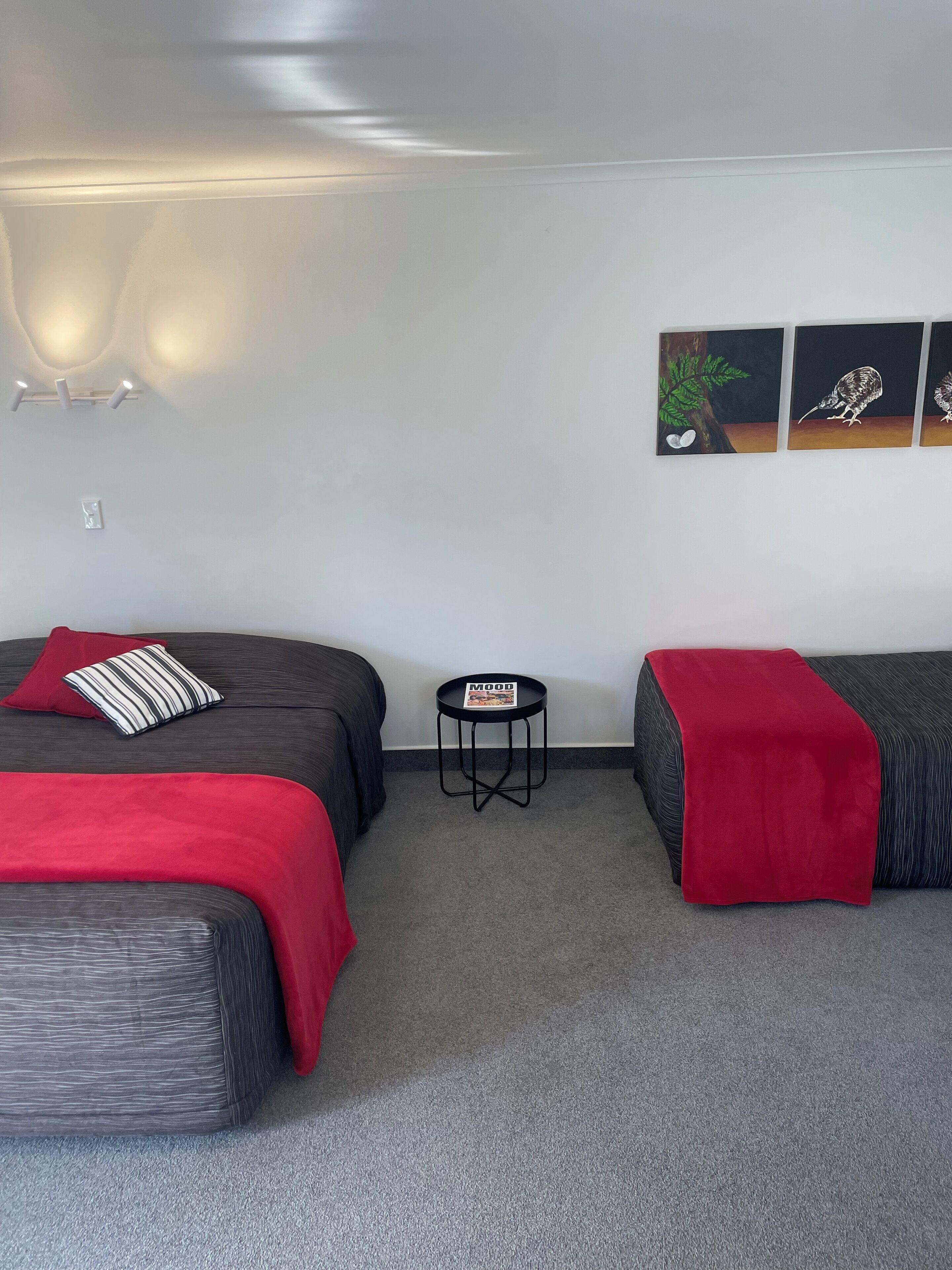 A hotel room with two beds, a small table, and wall art.