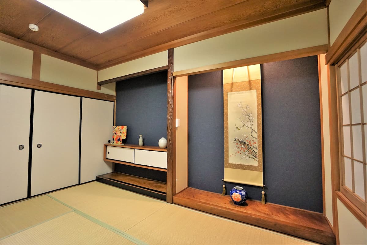Ein traditioneller japanischer Raum mit Tatami-Böden, Schiebetüren und einem Holzregal mit Dekoration.