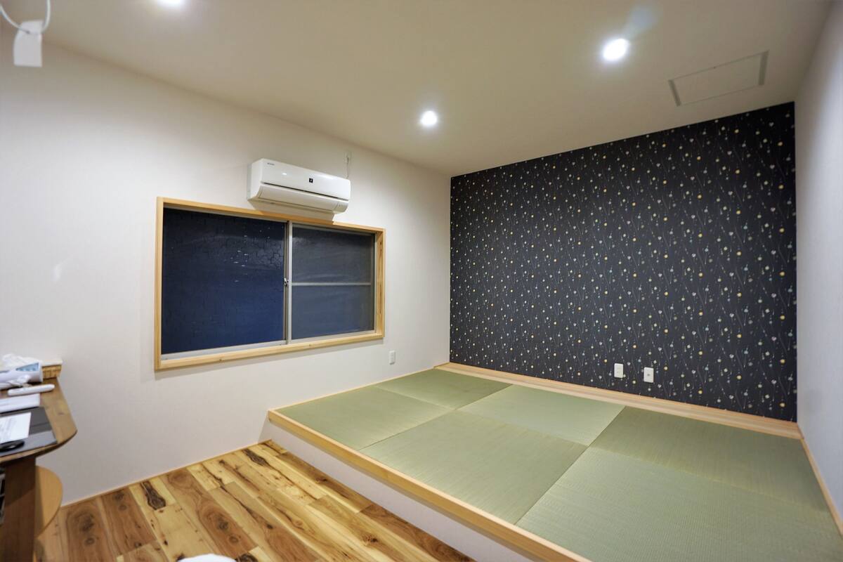 Ein Zimmer mit einem Schlafplatz auf Tatami-Matte, einem Fenster mit Ausblick und einer Wand mit Sternenmuster.