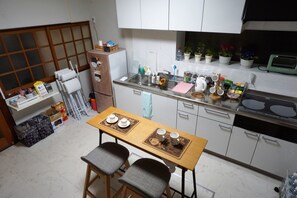 A compact kitchen with a dining table, two chairs, a refrigerator, a stove, and various kitchen items.