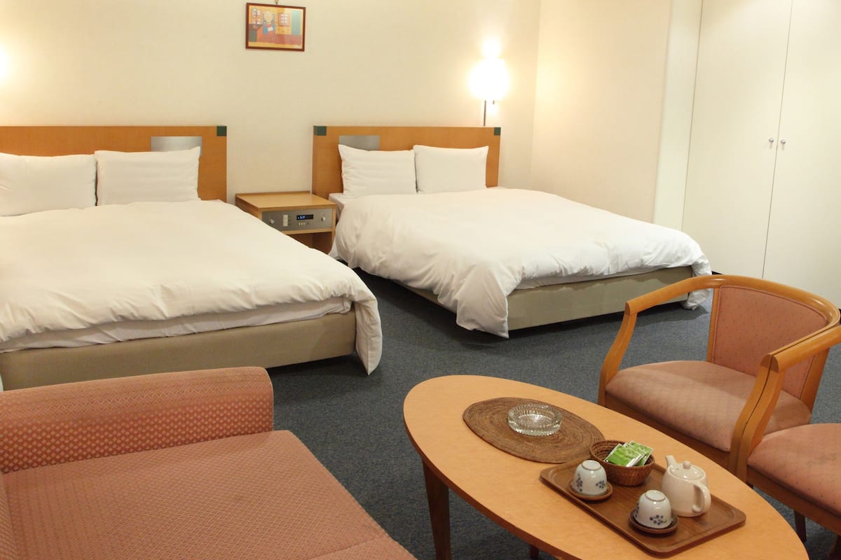 Quarto de hotel com duas camas, uma mesa pequena com chá e uma cadeira.
