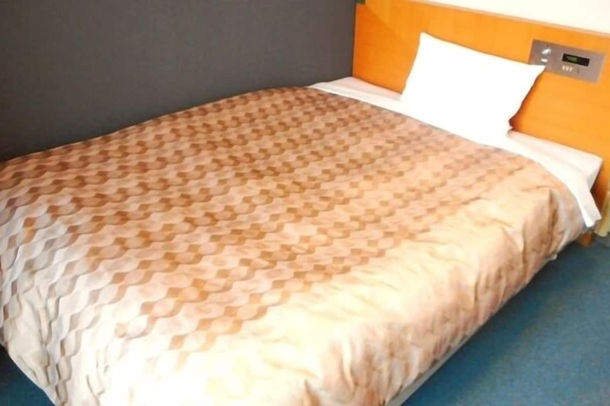 Uma cama com colcha estampada, travesseiro branco e cabeceira com visor digital.