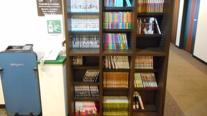 Una estantería llena de libros diversos y un carrito azul con un teléfono y una caja registradora.