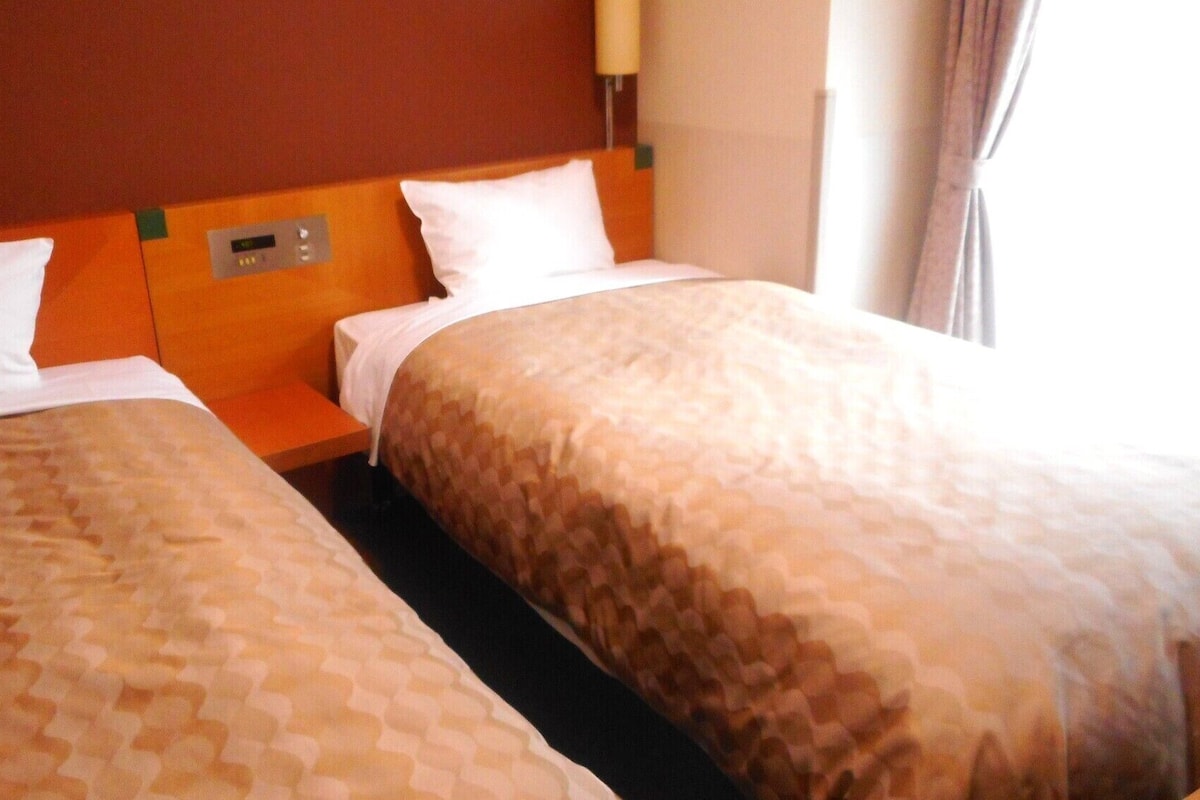 Quarto de hotel com duas camas, um painel de controle e uma janela com cortinas.