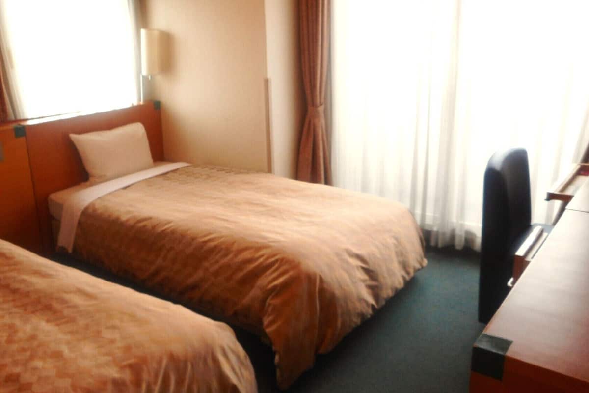 Quarto de hotel com duas camas, uma escrivaninha e uma cadeira.
