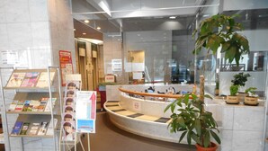 Zona de recepción con un mostrador curvo, folletos informativos y plantas en macetas.