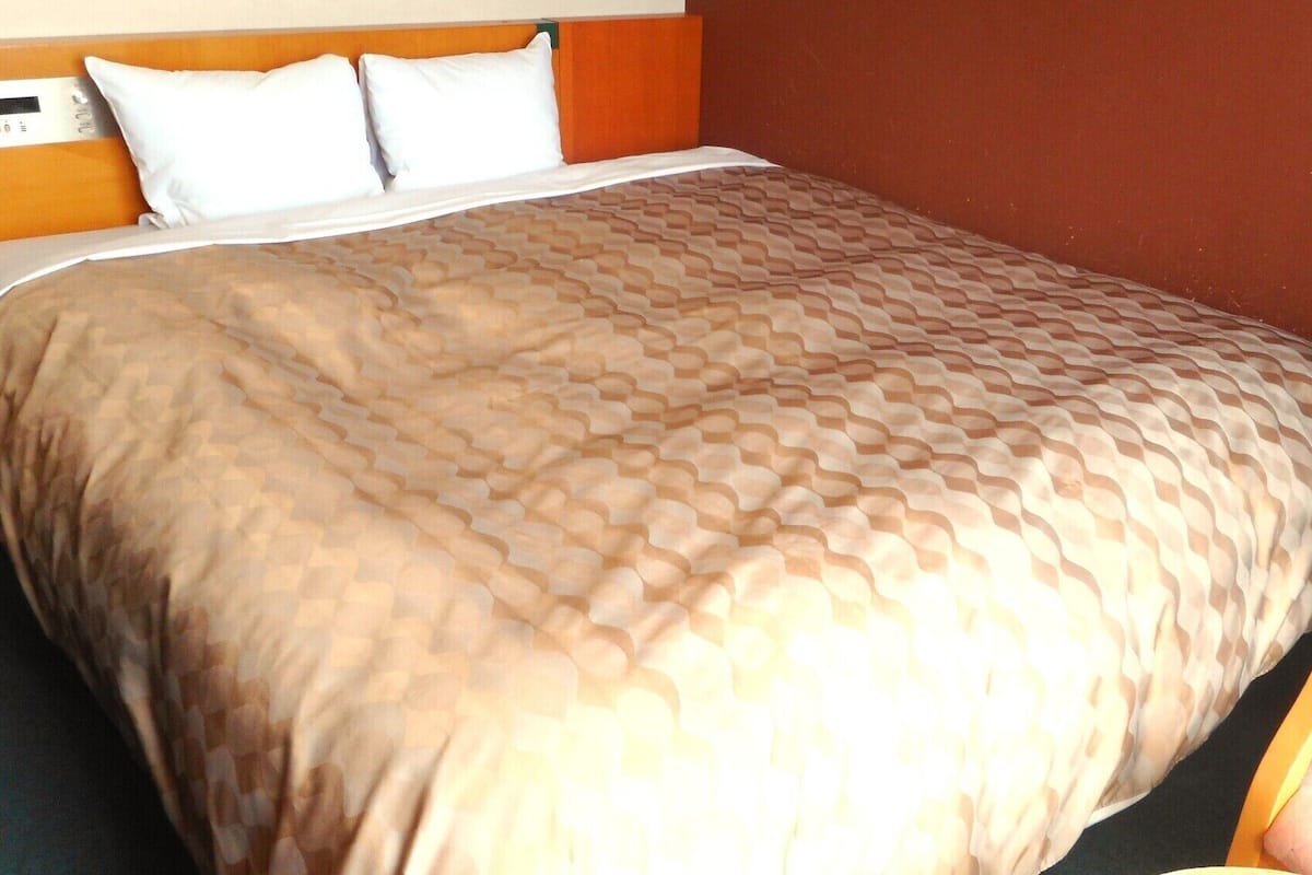 Quarto de hotel com cama, almofadas e cabeceira.