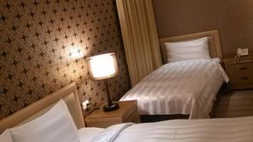 Habitación de hotel con dos camas, una mesita de noche con lámpara y un papel tapiz estampado.
