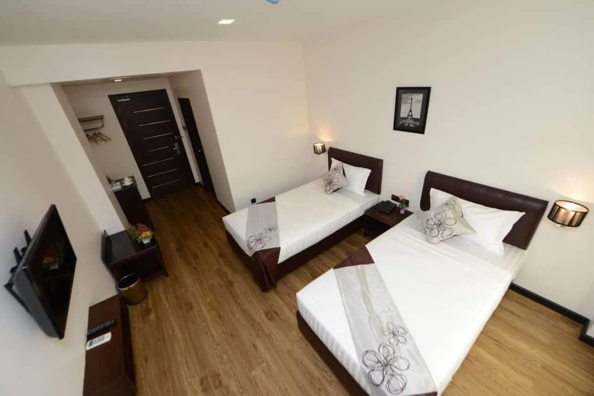 Ein Hotelzimmer mit zwei Betten, Holzboden, einem Fernseher, Nachttischen und einer Tür zu einem weiteren Raum.
