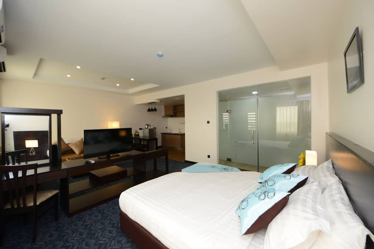 Ein Hotelzimmer mit Bett, Schreibtisch, Stuhl, Fernseher und einem durch eine Glaswand abgetrennten Badezimmer.
