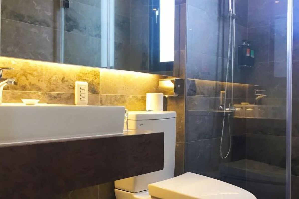 Un baño moderno con ducha envuelta en vidrio, un lavamanos blanco y un inodoro.