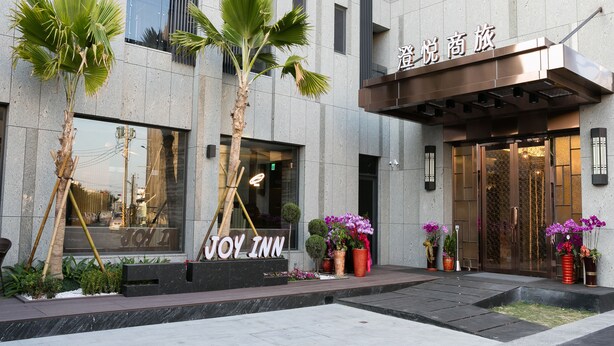 Entrada de un hotel con un cartel que dice "JOY INN" y una fachada de edificio moderna.