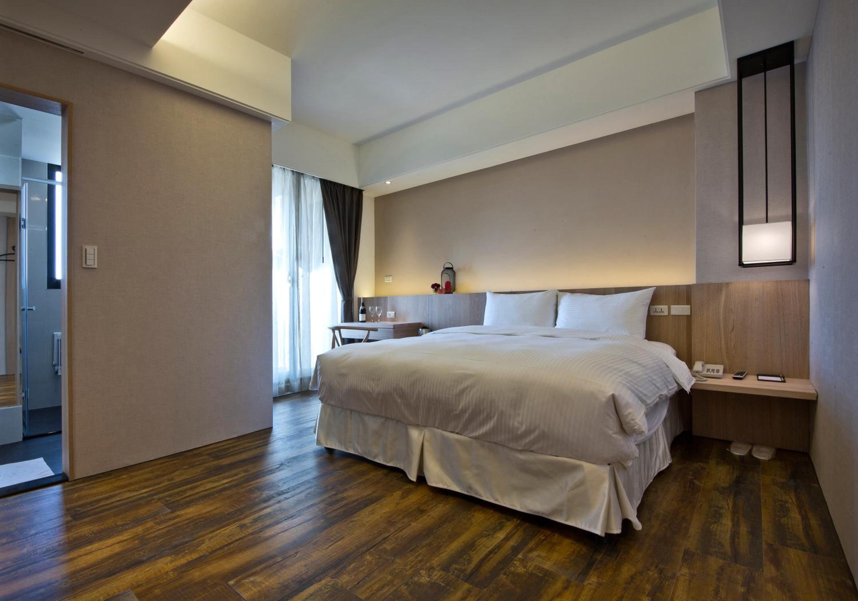 Una habitación de hotel con una cama grande, mesitas de noche, un espejo y vistas al pasillo.