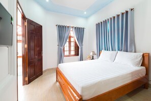 A bedroom with a wooden bed, a window with curtains, a nightstand, and a door. - Wings Bungalow (Phu Quoc)