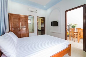 A hotel room with a bed, wooden wardrobe, a television mounted on the wall, and a dining area with chairs and a table. - Wings Bungalow (Phu Quoc)