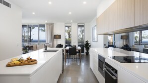 Una cocina moderna con una isla central, un área de comedor con mesa y sillas, y ventanas amplias que ofrecen vistas al exterior.