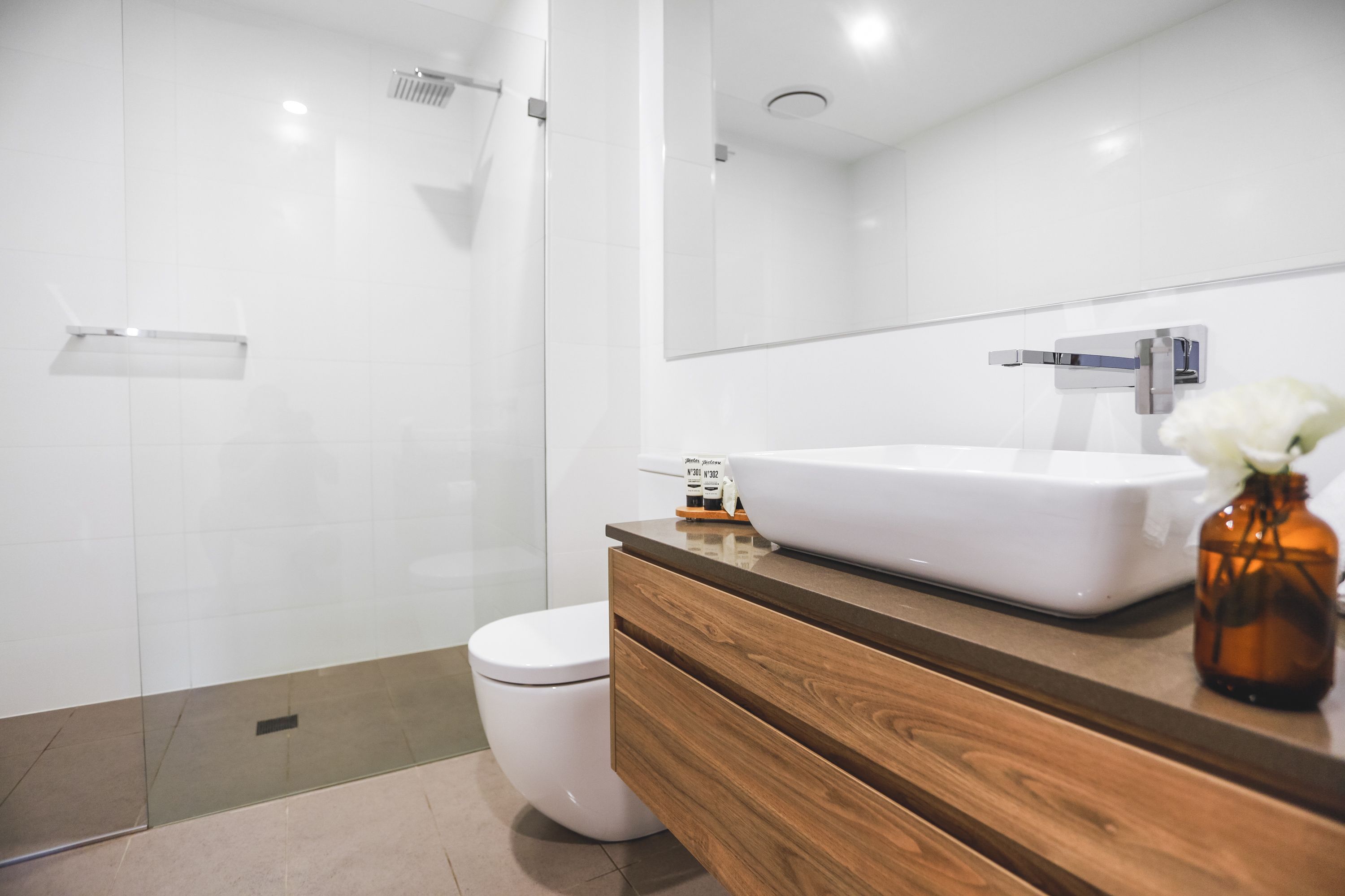 A modern bathroom with a white toilet, a wooden vanity, a white sink, and a large mirror.