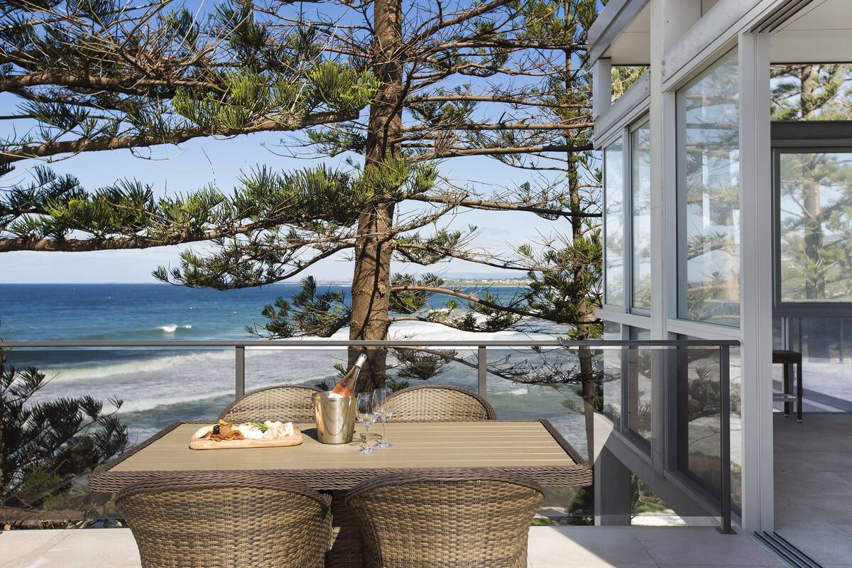 A balcony with wicker furniture, a bottle of champagne, and a glass, overlooking the ocean.