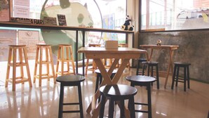 L’intérieur d’un café, avec des tabourets et des tables en bois, une grande fenêtre et une vue sur la rue.