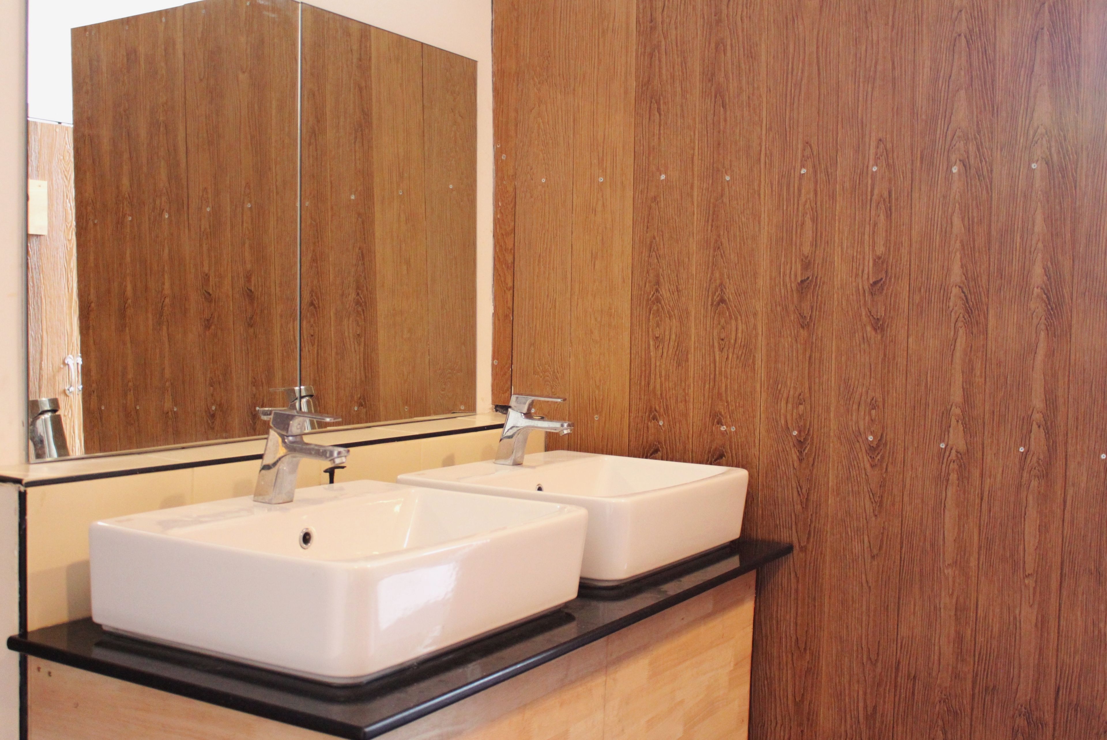 A bathroom with two white sinks, a large mirror, and wooden paneling.