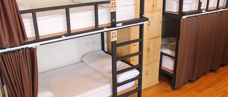 Una habitación tipo dormitorio con literas, armarios de madera y una cortina.