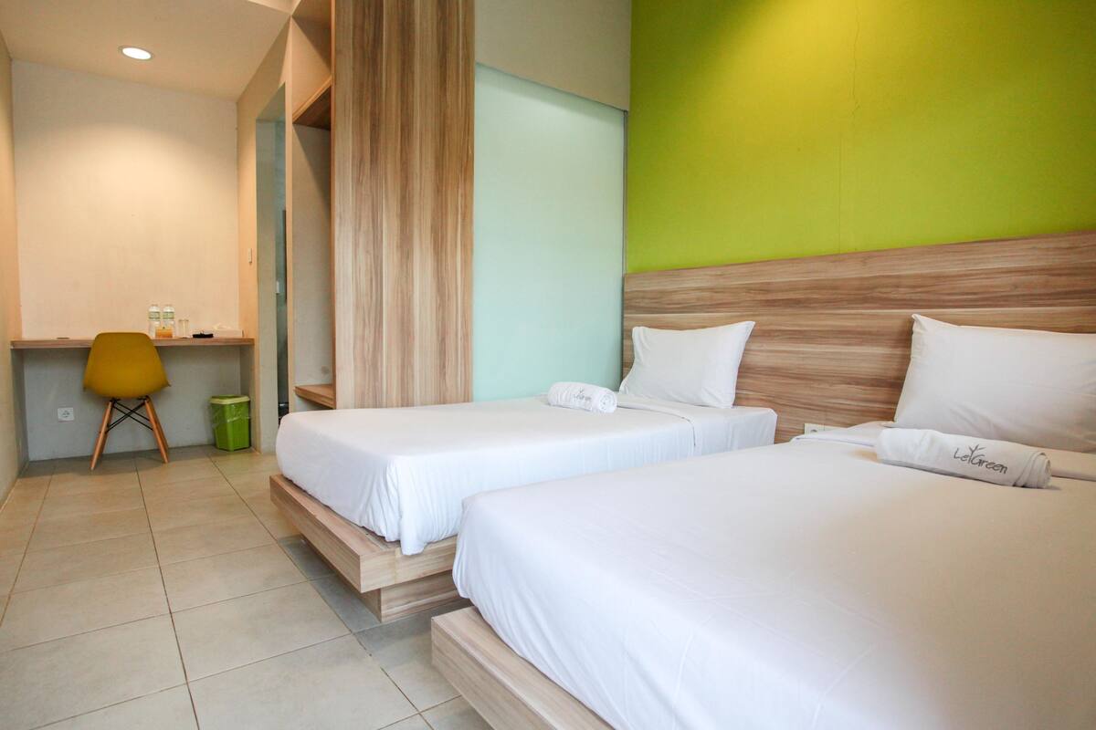 A hotel room with two single beds, a desk with a chair, and a green accent wall.