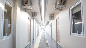 A long, narrow hallway with tiled floors, air conditioning units on the walls, and windows on both sides. - LeGreen Suite Supomo (Jakarta)