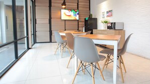 A modern dining area with a wooden table, grey chairs, and a television mounted on the wall. - LeGreen Suite Supomo (Jakarta)