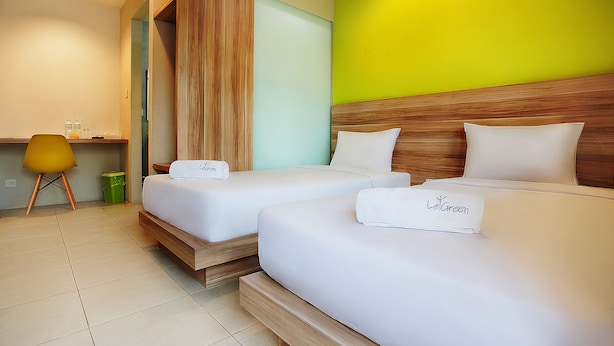 A hotel room with two beds, a wooden headboard, a green wall, and a yellow chair. - LeGreen Suite Supomo (Jakarta)