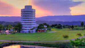 A modern hotel with a circular design, surrounded by a well-maintained golf course and a calm lake reflecting the building. - Hotel Azalea (Tsu)