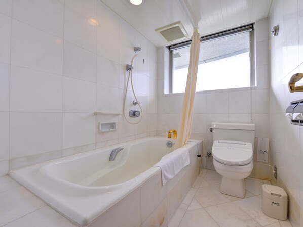 A modern bathroom with a bathtub, toilet, and a window.