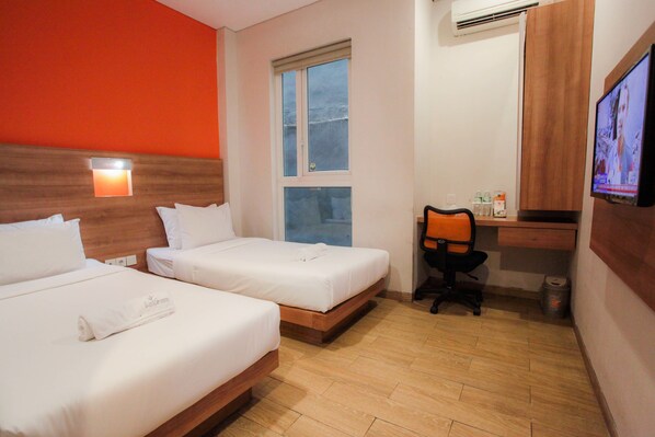 Habitación de hotel con dos camas individuales, un escritorio con silla, un televisor y una ventana.
