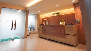 A reception desk with a wooden finish, a potted plant, and a wall-mounted air conditioner. - LeGreen Suite Kuningan (Jakarta)