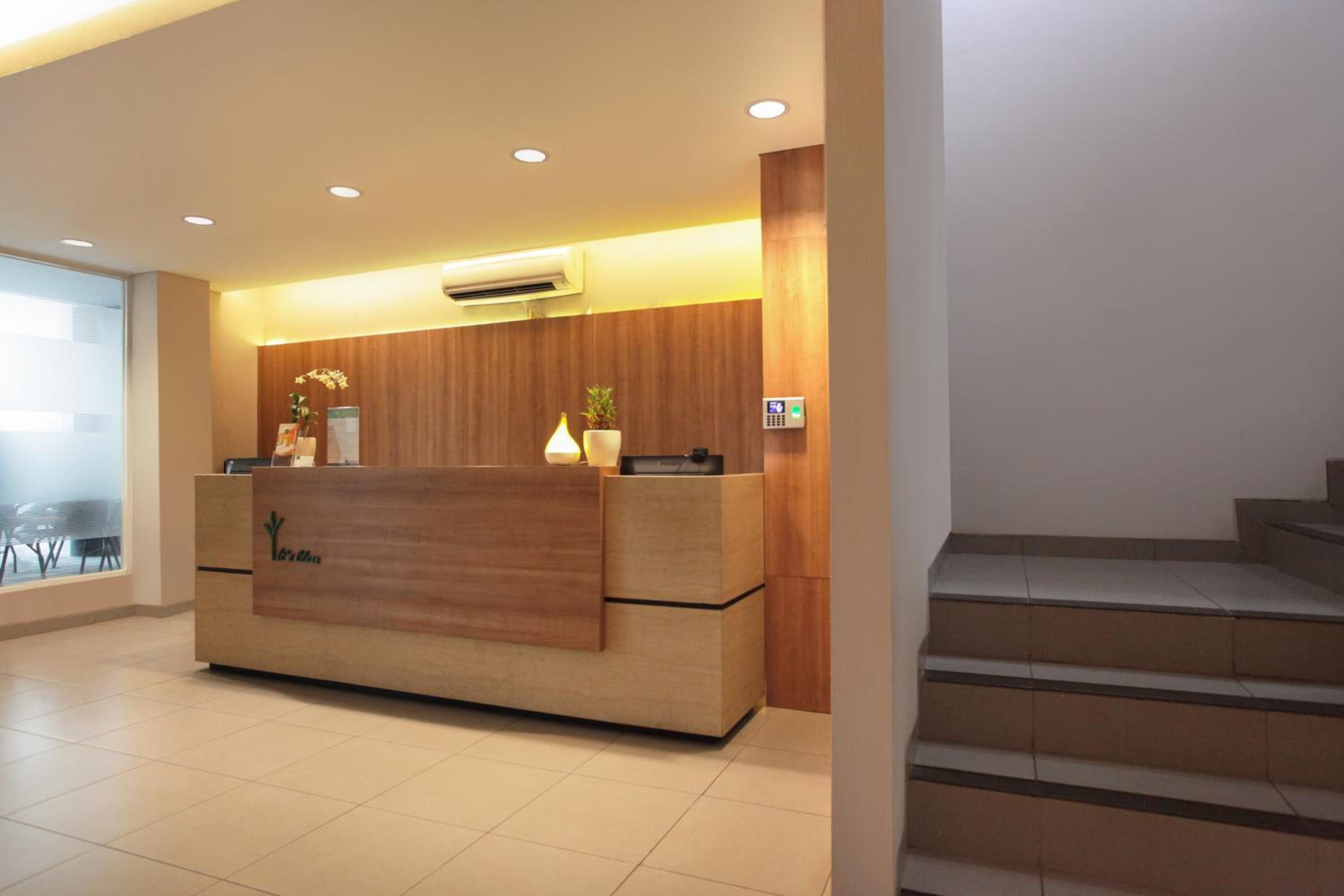 Un mostrador de recepción con detalles de madera, una pantalla digital y una planta en maceta.