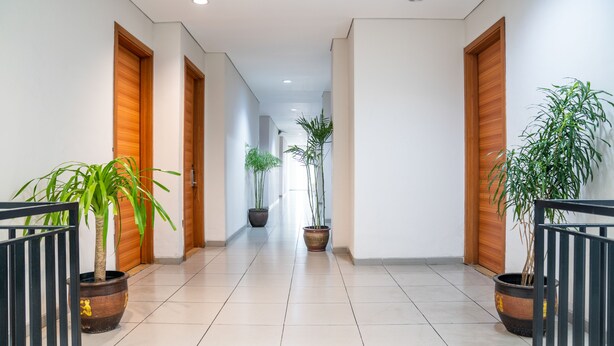 A hallway with wooden doors, potted plants, and a tiled floor. - LeGreen Suite Kuningan (Jakarta)