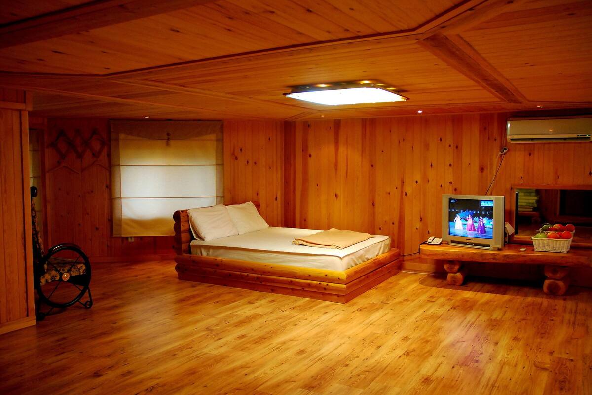 Una habitación de madera con una cama, un televisor y una mesita con fruta.