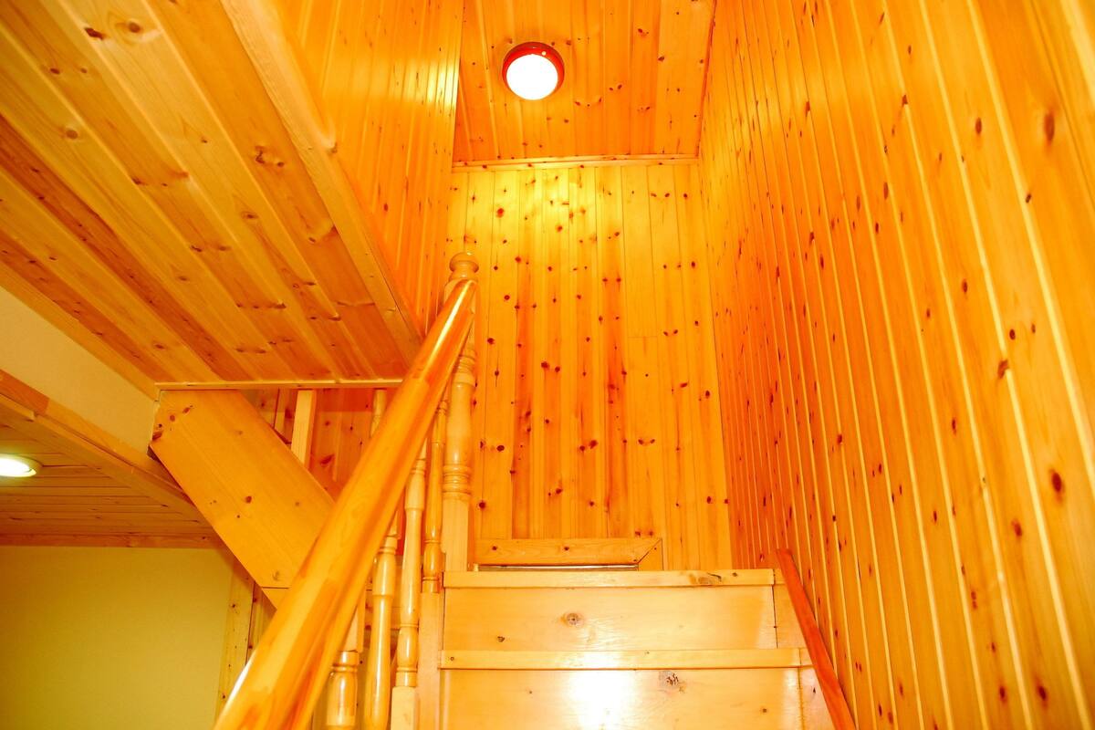 Una escalera de madera con barandilla que lleva a un ventanal circular en la parte superior.