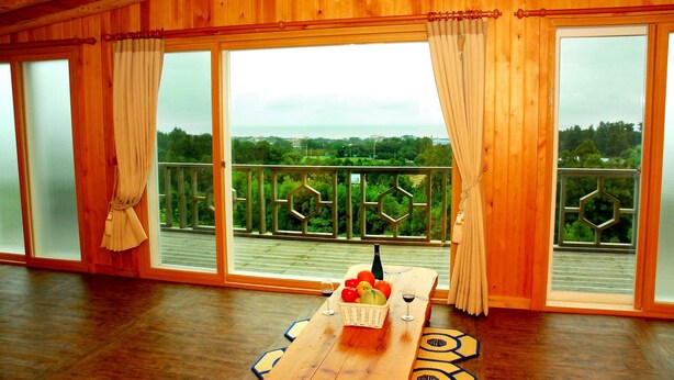 Une pièce en bois avec une grande porte-fenêtre coulissante donnant sur un balcon. Une table en bois, sur laquelle sont posés un panier de fruits et deux verres à vin, est placée au centre de la pièce.