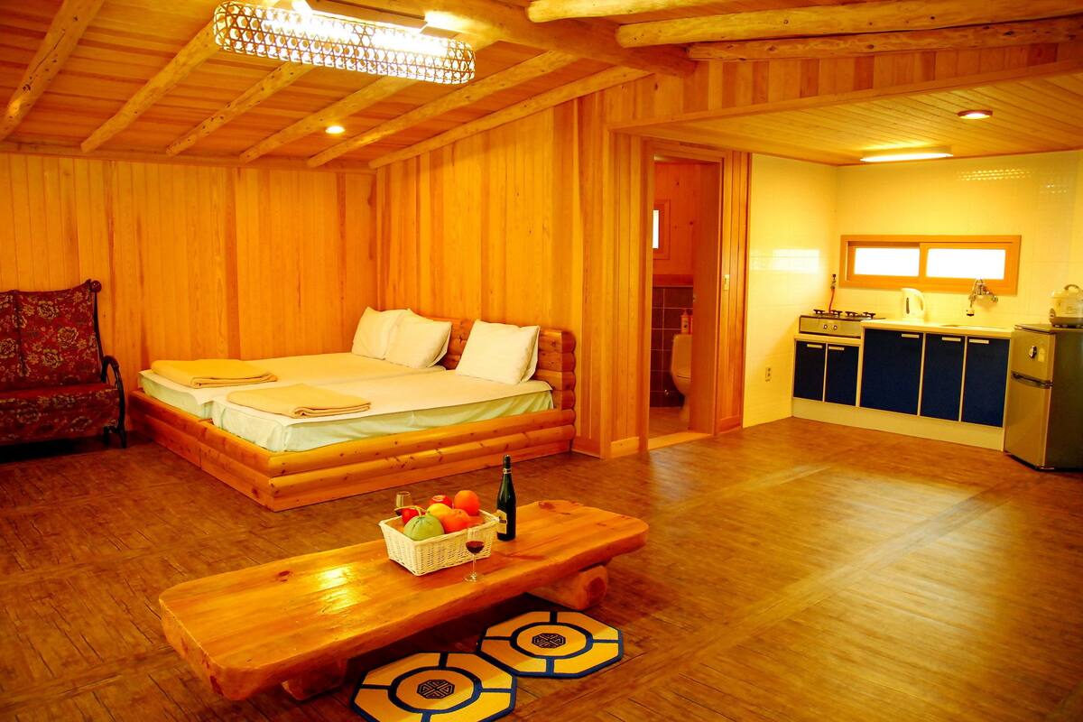 Una cabaña de madera con una cama grande, un banco de madera con fruta y una zona de cocina.