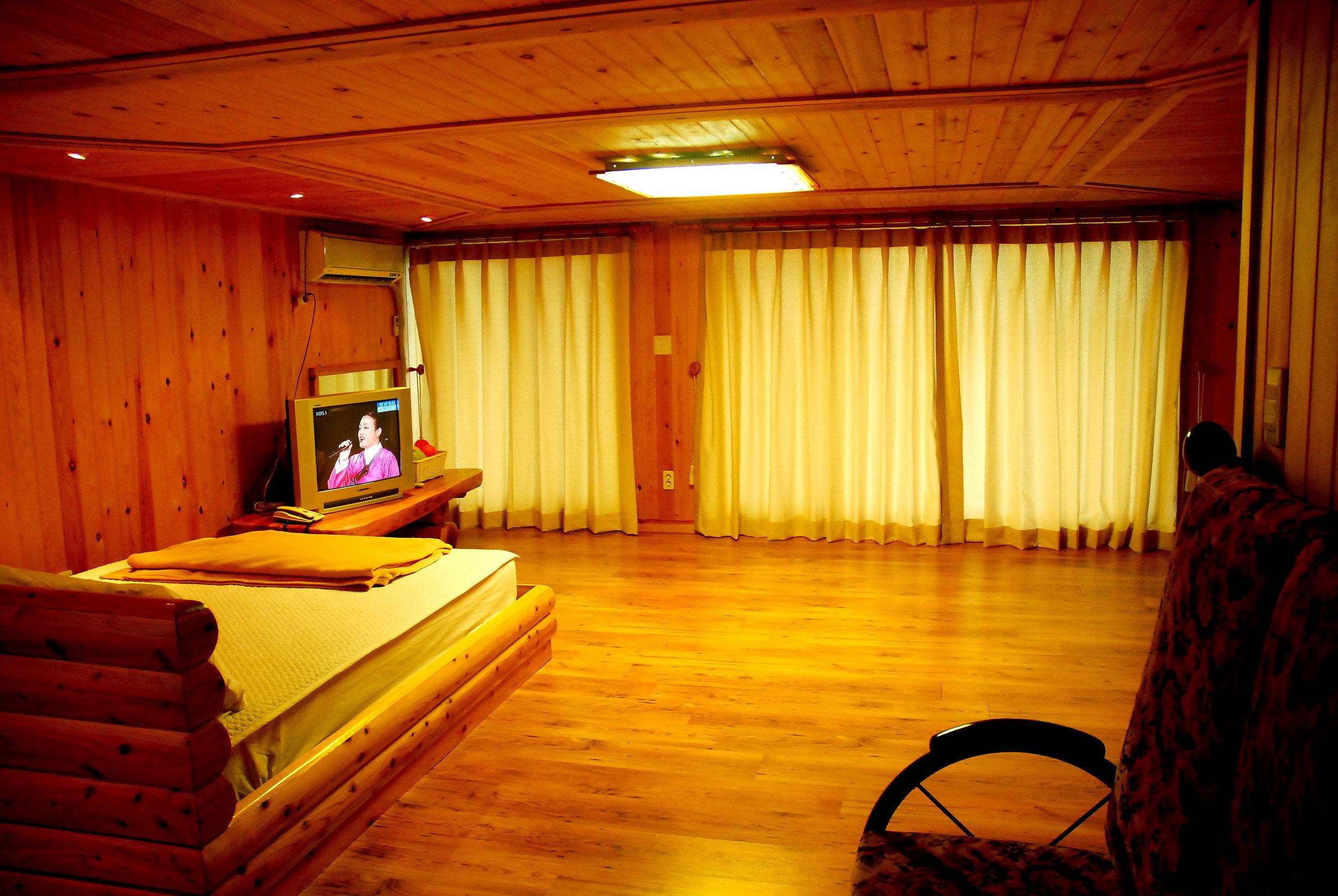 Una stanza in legno con un letto, una televisione e delle tende.