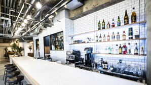 A modern bar with a long counter, bar stools, and shelves of liquor bottles. - HafH Fukuoka THE LIFE - Hostel (Fukuoka)