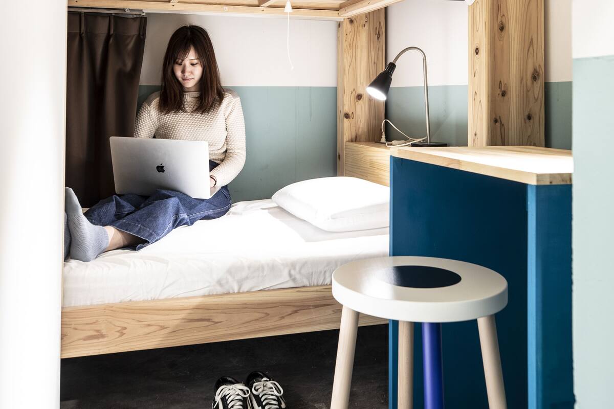 A bunk bed with a laptop on the lower bunk, a desk with a lamp, and a pair of shoes on the floor.