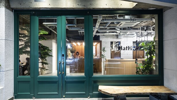A reception area with a green door, a wooden bench outside, and a visible interior with a counter and plants. - HafH Fukuoka THE LIFE - Hostel (Fukuoka)